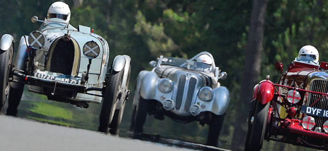 Three classic racing cars driving around the Le Mans circuit