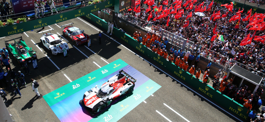 Fans celebrating on track as the winners of the 2022 24 Hours of Le Mans spray champagne on the podium